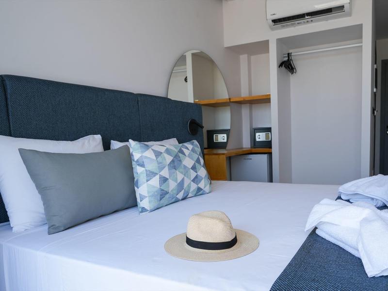 Schlafzimmer mit weißem Bett, blauen Kissen, Hut auf der Matratze und offenem Kleiderschrank.