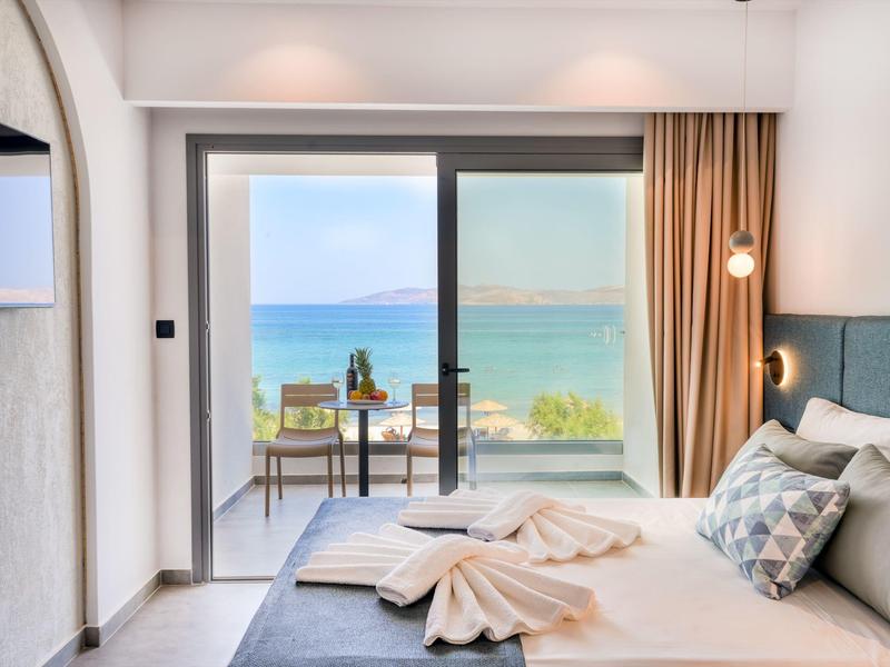 Helles Schlafzimmer mit großem Glasfenster, das auf einen Balkon und das blaue Meer blickt.