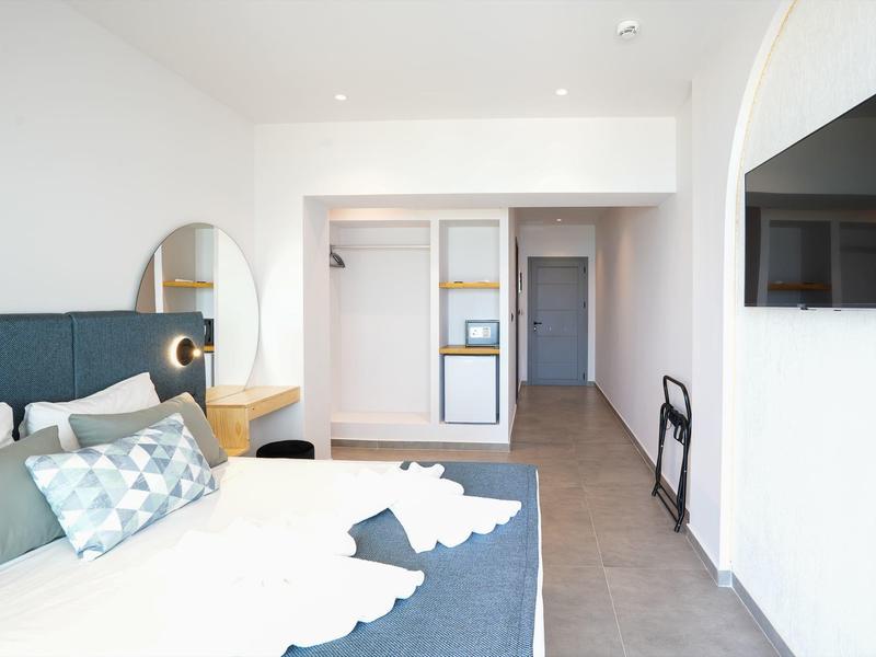 Hell eingerichtetes Schlafzimmer mit Doppelbett, runder Spiegel und offenem Kleiderschrank.