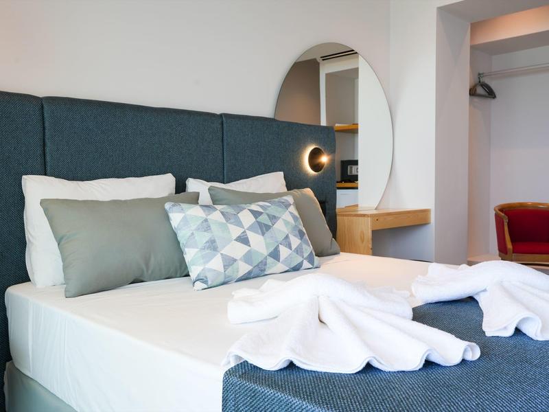 Modernes Schlafzimmer mit grauem Polsterbett, weißer Bettwäsche und geometrischem Zierkissen.