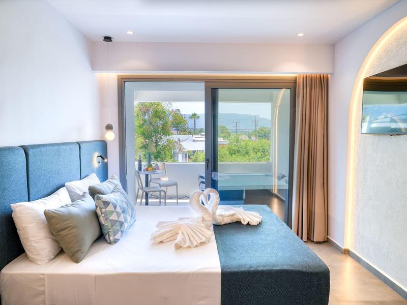 Helles Schlafzimmer mit großem Fenster, blauem Bett, weißen Kissen und Balkon mit Seeblick.