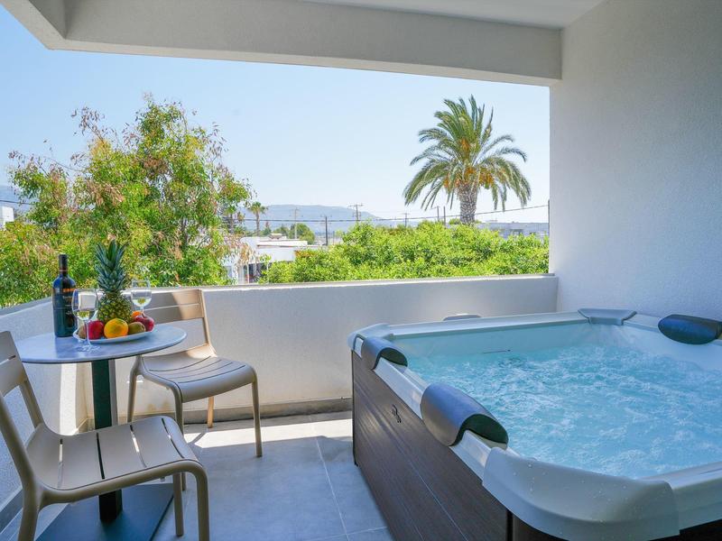 Balkon mit Whirlpool, zwei Stühlen, Tisch mit Obst und Wein, Blick auf Palmen und Meer.