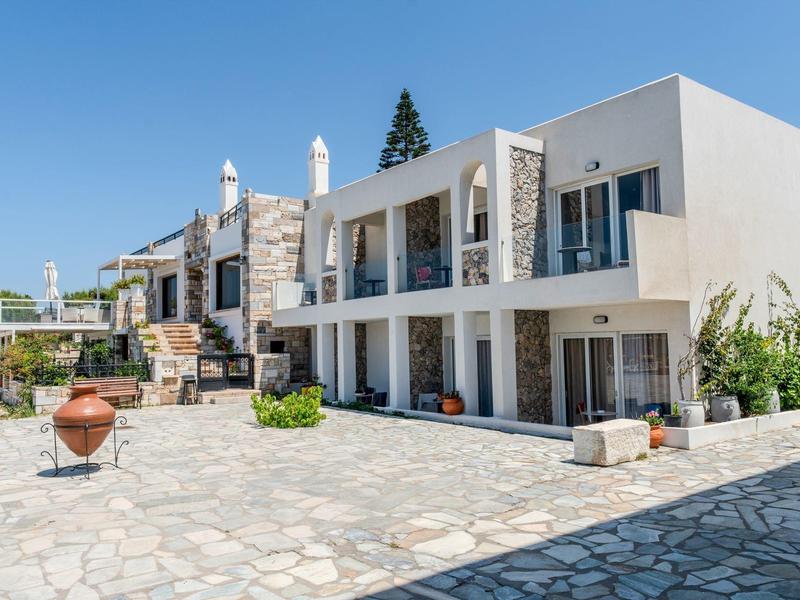 Modernes Hotelgebäude mit Balkon und Steinmauer, Innenhof mit Steinboden und Sonnenschein.