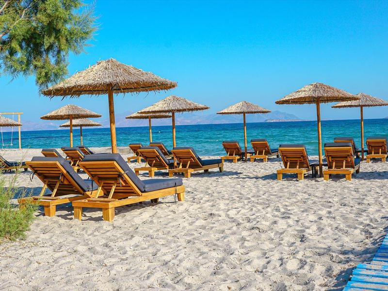Strand mit Liegestühlen und Strohhütten unter blauem Himmel am ruhigen Meer.