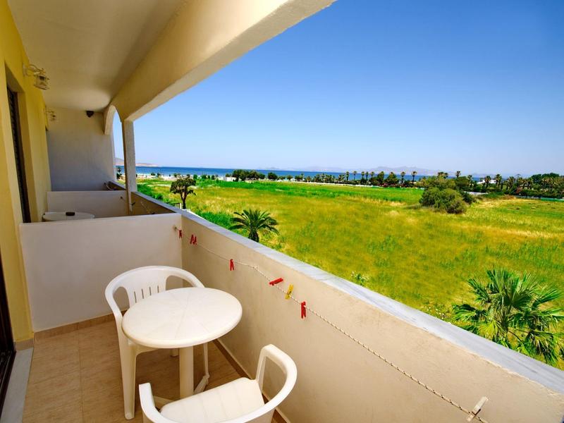 Balkon z białym stołem i krzesłami z widokiem na zielony ogród i niebieskie niebo.