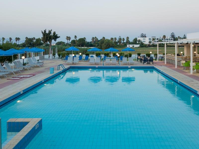 Duży zewnętrzny basen z niebieską wodą, otoczony leżakami i parasolami.