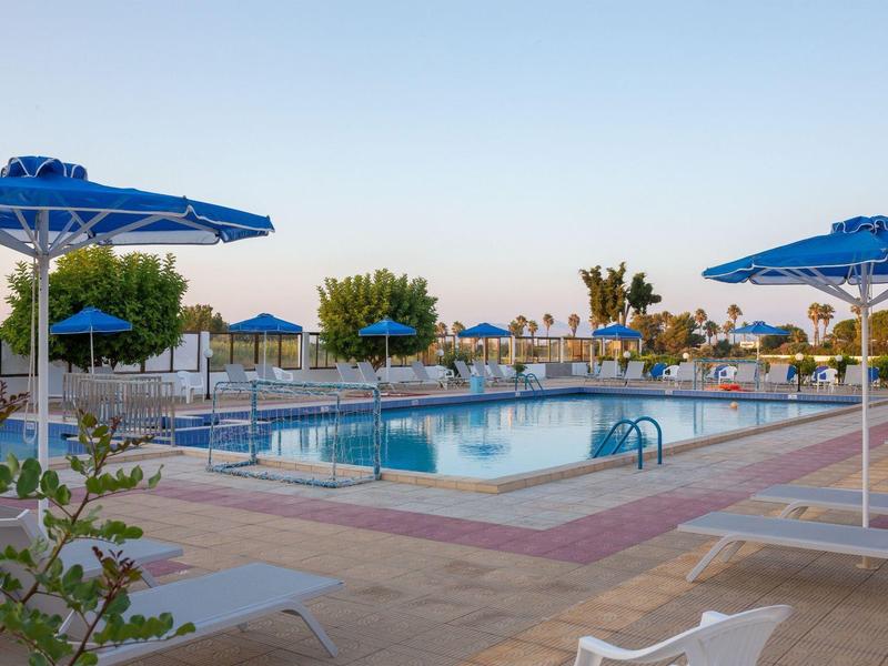 Duży basen na świeżym powietrzu z niebieskimi parasolami i leżakami pod czystym niebem.