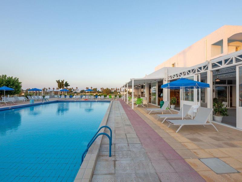 Duży basen obok nowoczesnego budynku hotelu z parasolami i leżakami pod czystym niebem.