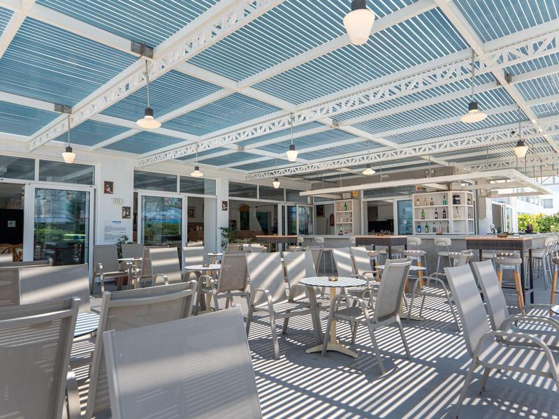 Jasny zadaszony taras z wieloma pustymi krzesłami i stołami w nowoczesnym hotelu.