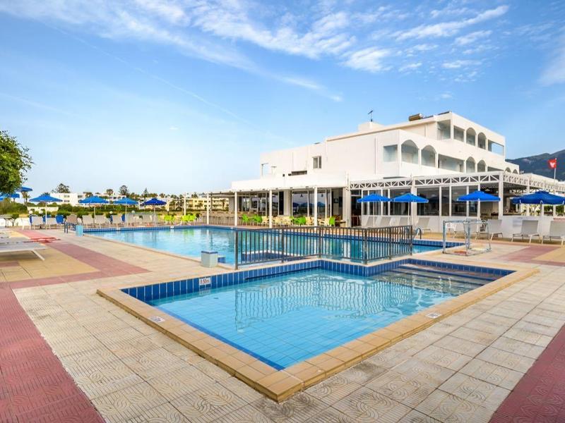 Duży basen na zewnątrz z leżakami i parasolami obok budynku hotelu pod niebieskim niebem.