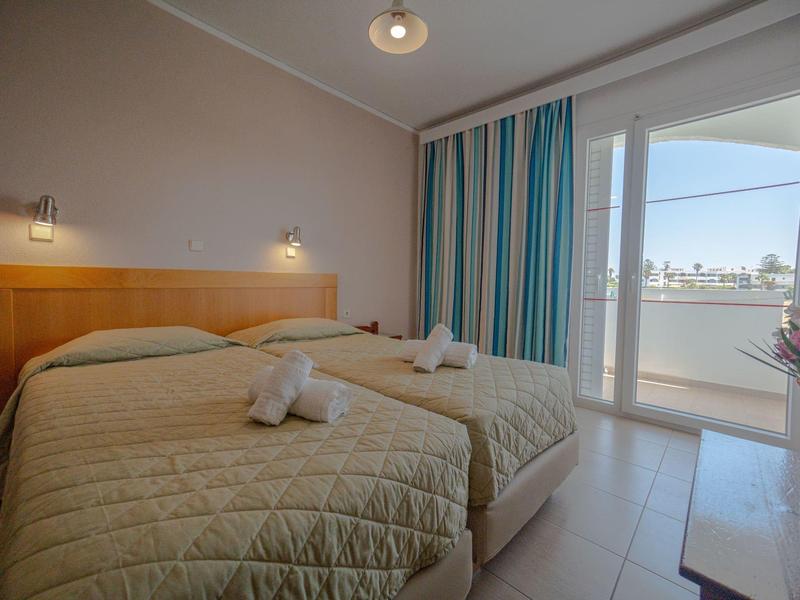 Pokój hotelowy z dwoma łóżkami pojedynczymi, drzwiami na balkon i nowoczesnym, jasnym wnętrzem.