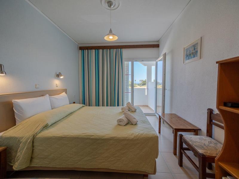 Jasny pokój hotelowy z łóżkiem podwójnym, balkonem i widokiem na morze.