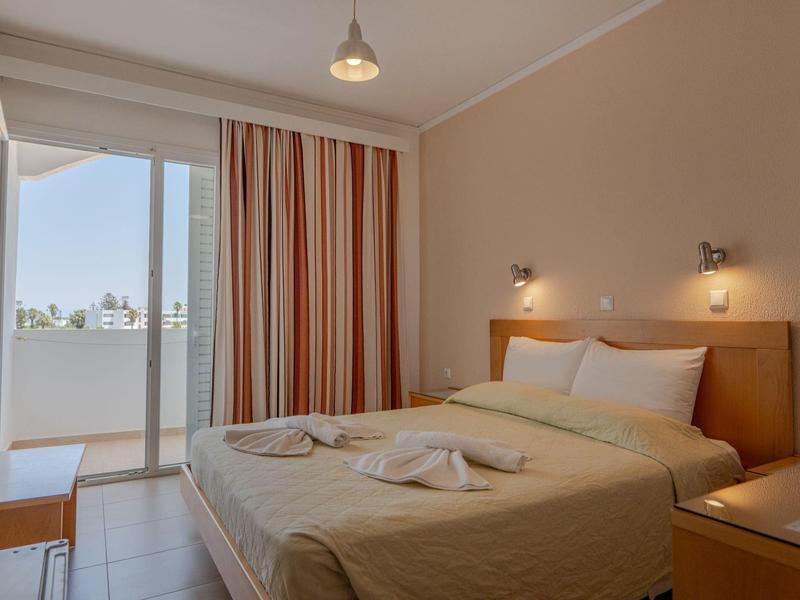 Przytulny pokój hotelowy z podwójnym łóżkiem, stolikami nocnymi i balkonem z widokiem.