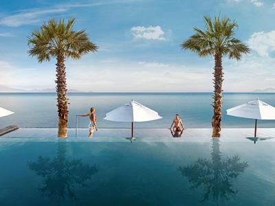 Infinity pool overlooking the sea, two palm trees and umbrellas on a sunny day