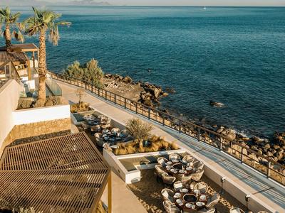 Terrasse mit Tischen und Stühlen an der Küste mit Blick auf das Meer und Palmen.