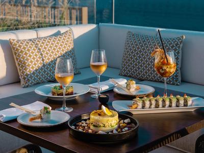 Gemütliche Outdoor-Lounge mit braunem Holztisch, Wein, Cocktails und Sushi-Platten.