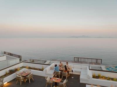 Drei Personen sitzen in einer modernen Außenterrasse mit Meerblick und weißen Sitzmöbeln.