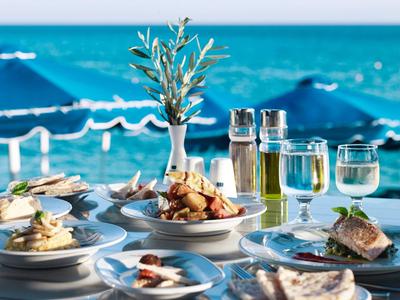 Stůl s mořskými plody a nápoji u moře pod jasnou modrou oblohou.