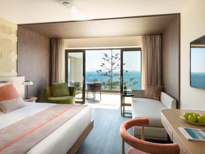 Moderní hotelový pokoj s výhledem na moře, manželskou postelí, posezením a balkonem.