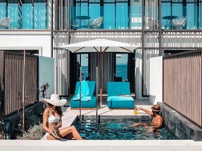 Moderní hotelový bazén s dvěma ženami relaxujícími u vody a lehátky ve světlé tyrkysové.