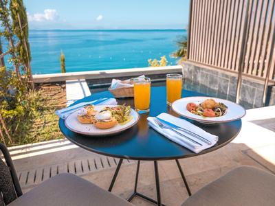 Stůl se snídaní a nápoji na balkoně s výhledem na moře.