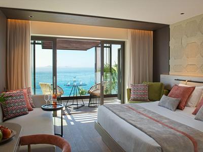 Modernes Hotelzimmer mit großem Bett, Sitzbereich und Meerblick durch die Panoramascheibe.