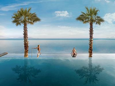 Infinity bazén se dvěma palmami s výhledem na klidný oceán a modrou oblohu.