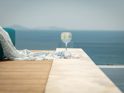 Sklenice na koktejl stojí na okraji bazénu s výhledem na moře a jasnou oblohu.