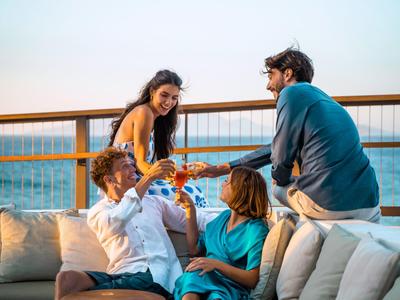 Vier Freunde genießen gesellig Zeit auf einem Balkon mit Meerblick bei Sonnenuntergang.