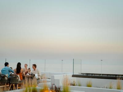 Gruppe sitzt draußen in Café mit Blick auf das Meer bei ruhigem Abendlicht.