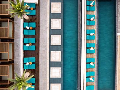 Vogelperspektive auf Hotelpool mit blauen Liegestühlen und Palmen an der Seite.