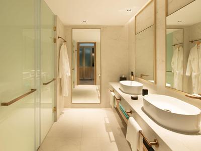 Baño moderno de hotel con dos lavabos ovalados, espejos grandes y decoración beige.