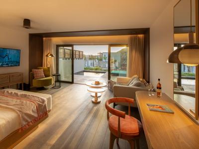 Amplia habitación de hotel con cama doble, escritorio y vista a terraza con lago.