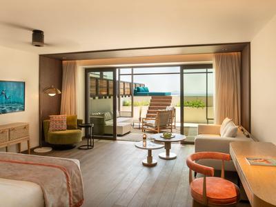 Habitación de hotel luminosa con área de estar, escritorio y vista a la terraza y paisaje.
