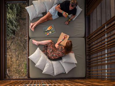 Dos personas relajándose en un gran sofá gris en una habitación de madera con vista a la vegetación.