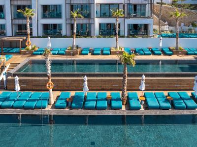 Hotel moderno con varias piscinas, tumbonas azules acolchonadas y palmeras.