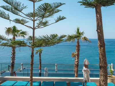 Moderna terraza de hotel con cojines turquesa, palmeras y vista al mar azul.