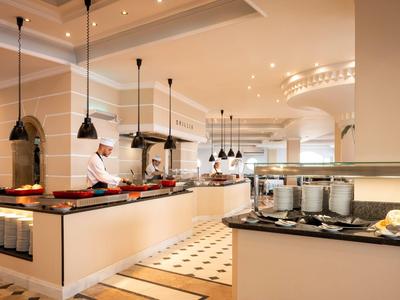 Bufé de hotel moderno y luminoso con estación de cocina y exhibición de alimentos en ambiente elegante.