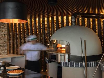 Pizzero moderno trabajando en una cocina de hotel elegante con horno de piedra.