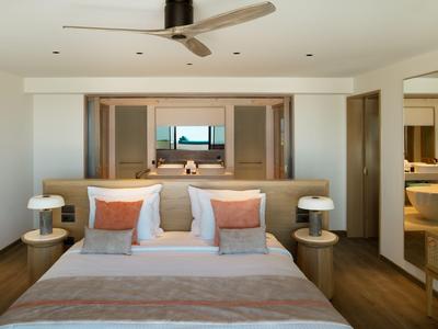 Habitación de hotel moderna con cama doble, ventilador de techo y vista al mar a través de puertas abiertas.