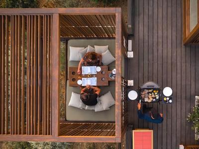 Vista aérea de una zona exterior con sofá y camarero con bandeja junto a una moderna casa de jardín de madera.