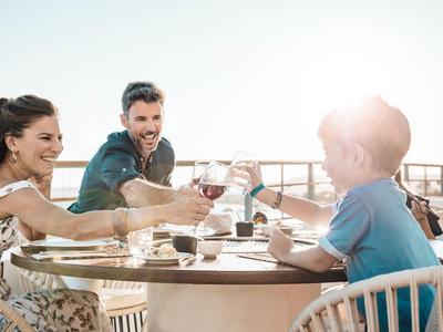Familia disfruta de un día soleado en la terraza del hotel con bebidas.