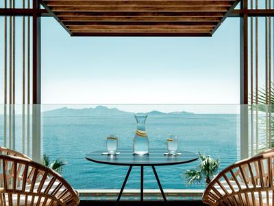 Vista al mar desde un balcón con barandilla de vidrio y mesa con jarra y vasos.