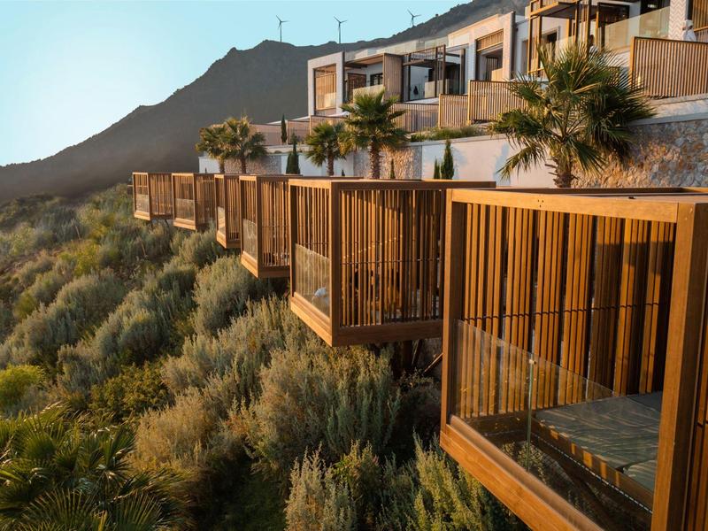 Balkony pokojů resortu s výhledem na bujnou zeleň a horskou krajinu při západu slunce.