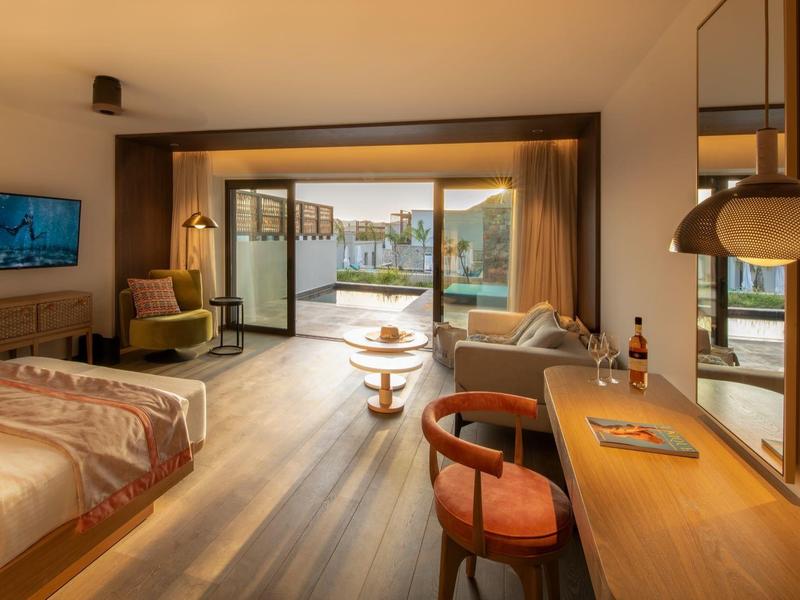 Světý hotelový pokoj s manželskou postelí, posezením a velkým oknem s výhledem na hory.