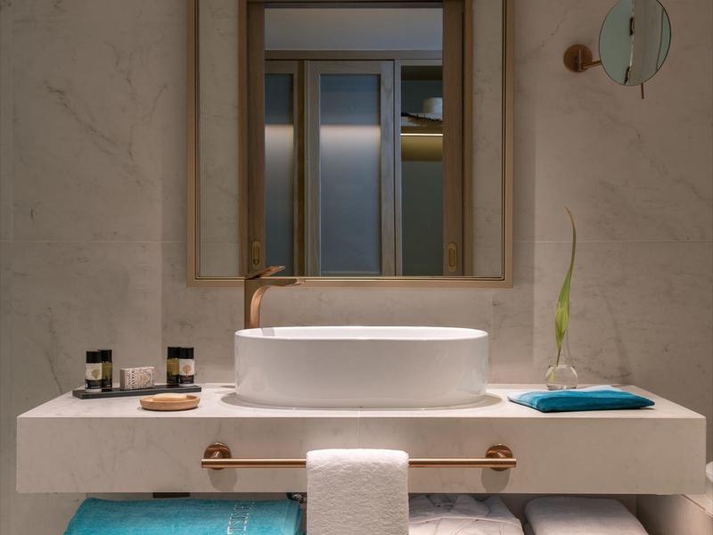 Moderní koupelna s velkým zrcadlem, umyvadlem, ručníky a pantoflemi.