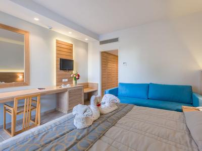 Modernes Schlafzimmer mit hellen Wänden, blauer Couch, großem Spiegel und Holzdetails am Schreibtisch.