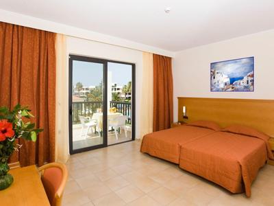 Hell eingerichtetes Hotelzimmer mit Doppelbett, großem Fenster und Balkonblick auf Stadt.
