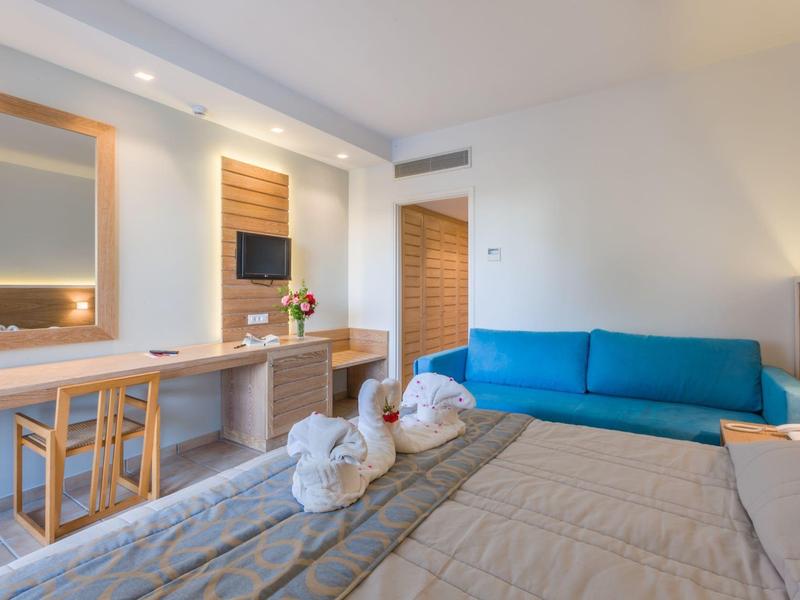 Moderní hotelový pokoj s postelí, modrou pohovkou a pracovním koutem se židlemi a zrcadly.