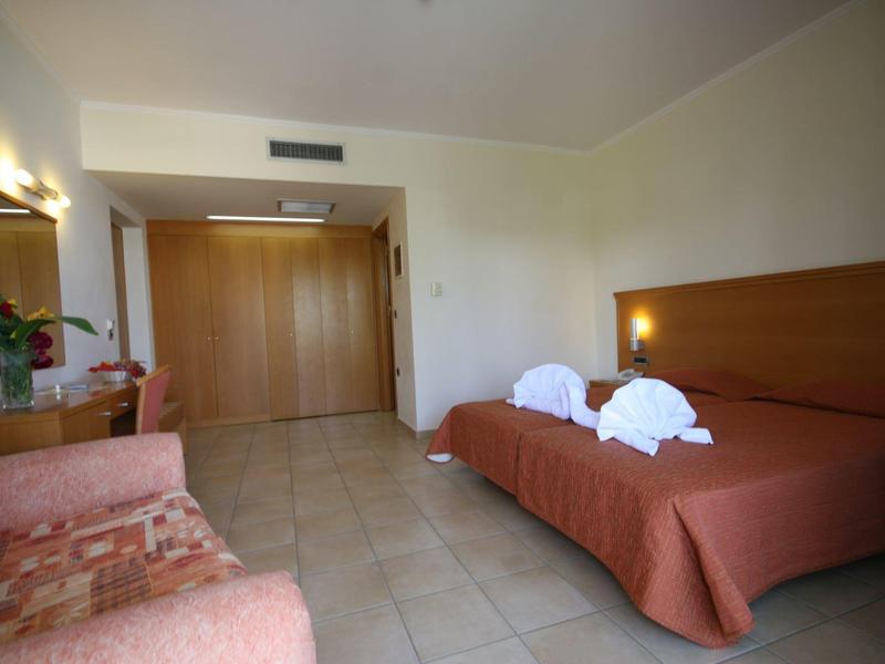 Hotelový pokoj s manželskou postelí, dvěma ručníkovými figurkami a křesly u bílé stěny.